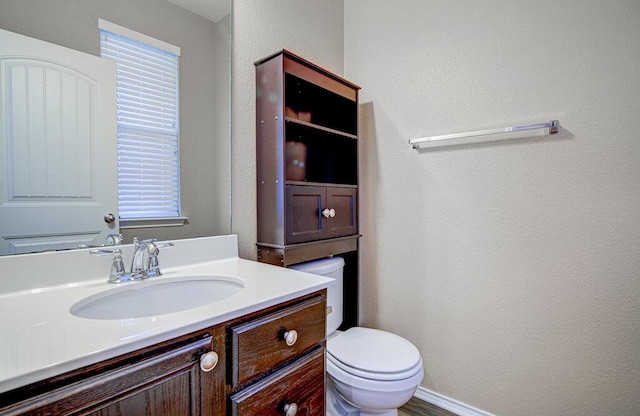 bathroom with a textured wall, vanity, and toilet