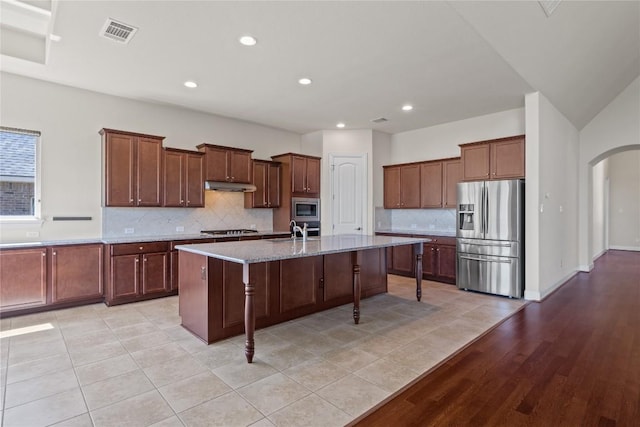 118 Bluehaw Dr, Georgetown, TX 78628 - kitchen with stainless steel appliances, a sink, under cabinet range hood, arched walkways, and decorative backsplash
