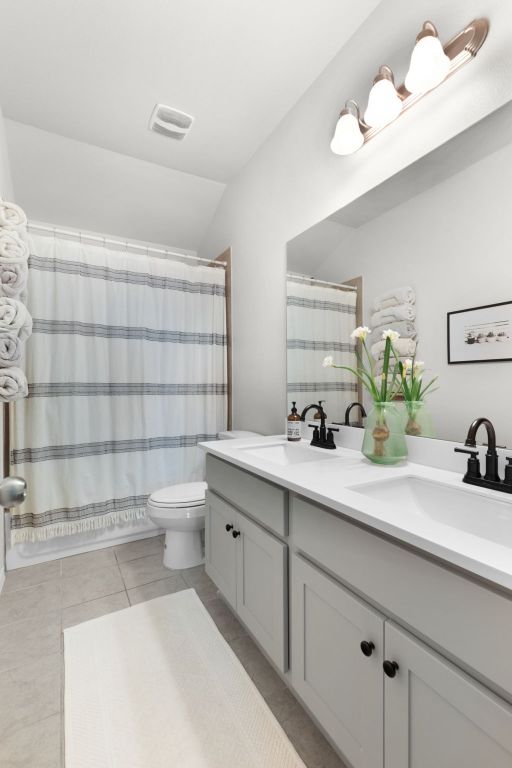 bathroom featuring tile patterned flooring, double vanity, a sink, and toilet