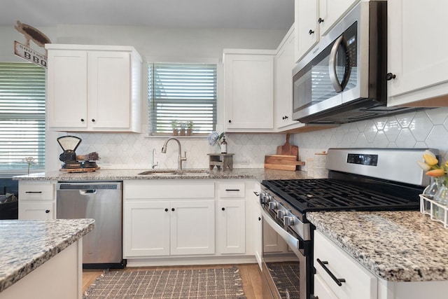 kitchen with tasteful backsplash, a sink, white cabinetry, light stone countertops, and stainless steel appliances