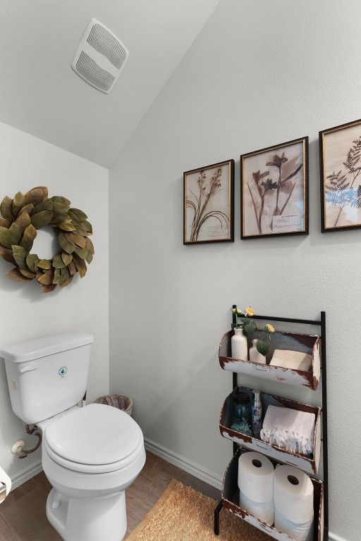 bathroom with baseboards, toilet, visible vents, lofted ceiling, and wood finished floors