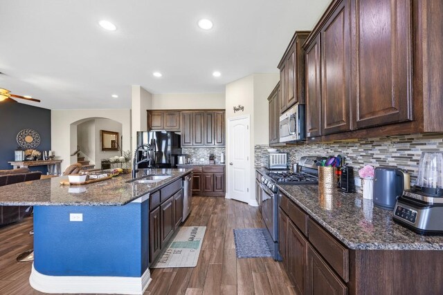 kitchen featuring appliances with stainless steel finishes, a sink, arched walkways, dark stone counters, and backsplash