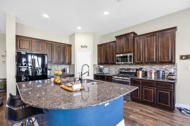 kitchen featuring stainless steel appliances, a sink, a breakfast bar, wood finished floors, and dark brown cabinetry