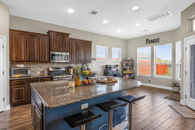 kitchen with stainless steel appliances, dark wood finished floors, healthy amount of natural light, recessed lighting, and a kitchen bar