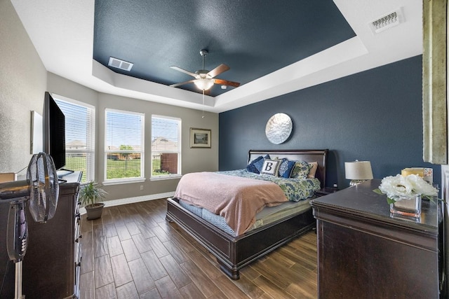 bedroom with a tray ceiling, baseboards, dark wood-style flooring, and a ceiling fan