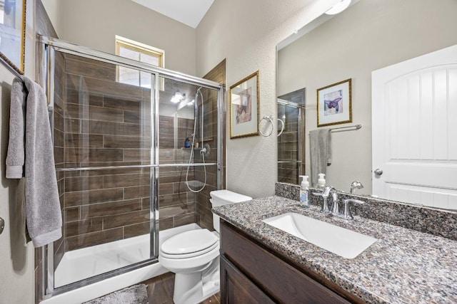 bathroom with a shower stall, toilet, vanity, and a textured wall