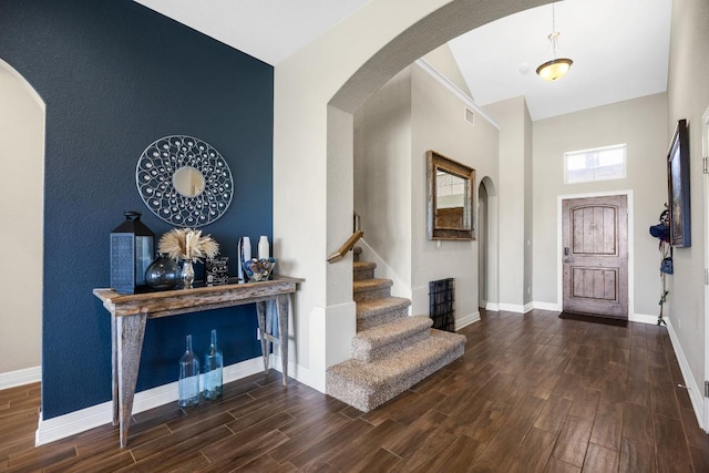 entryway with wood finished floors, baseboards, arched walkways, a high ceiling, and stairway
