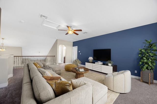 carpeted living room with ceiling fan, baseboards, attic access, vaulted ceiling, and arched walkways