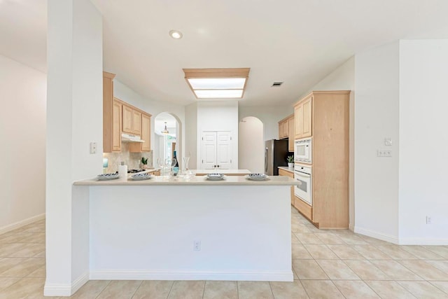 2709 Quiet Moon Trl, Cedar Park, TX 78613 - kitchen featuring light brown cabinets, arched walkways, white appliances, under cabinet range hood, and a peninsula