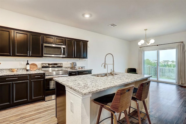 14209 Jeannette Rankin Rd, Manor, TX 78653 - kitchen with appliances with stainless steel finishes, a breakfast bar, a sink, light stone countertops, and a kitchen island with sink