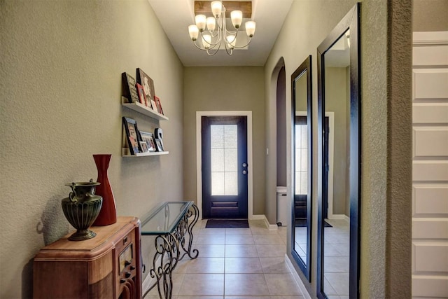 foyer with baseboards, arched walkways, a chandelier, a textured wall, and light tile patterned flooring
