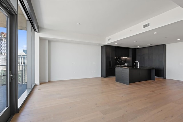44 E Ave Unit 4302, Austin, TX 78701 - kitchen featuring modern cabinets, dark cabinets, light wood-style flooring, dark countertops, and a kitchen island with sink