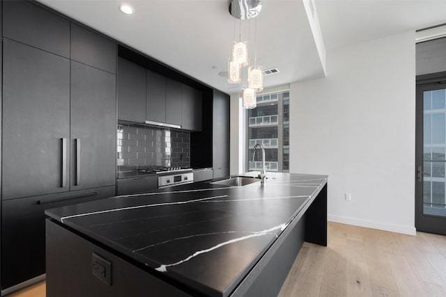 44 E Ave Unit 2307, Austin, TX 78701 - kitchen featuring a sink, light wood-type flooring, tasteful backsplash, decorative light fixtures, and an island with sink