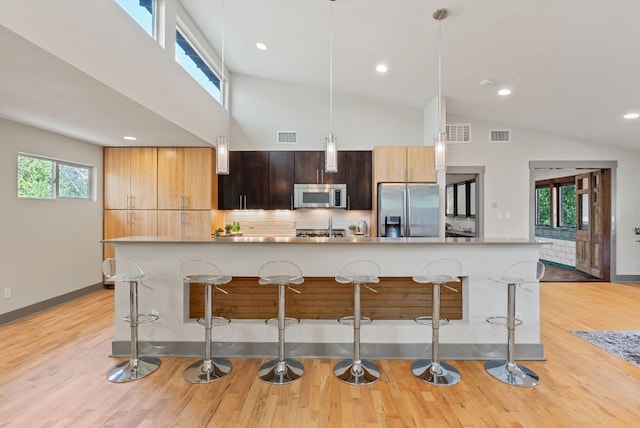 5607 Jim Hogg Ave, Austin, TX 78756 - kitchen with appliances with stainless steel finishes, a kitchen bar, light countertops, a large island with sink, and light wood-type flooring