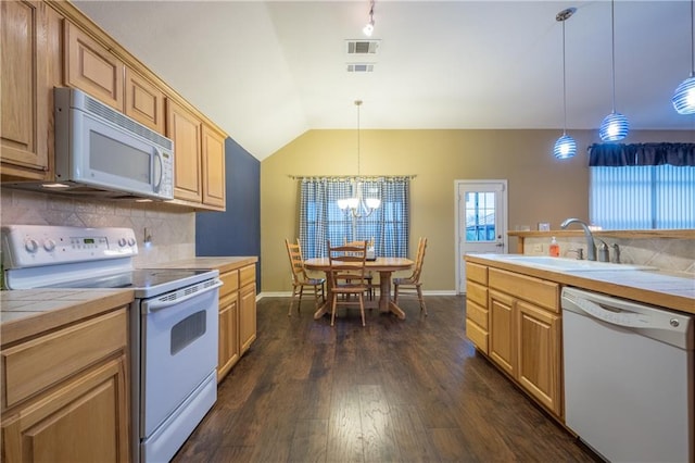 kitchen featuring white appliances, vaulted ceiling, a sink, decorative backsplash, and tile counters