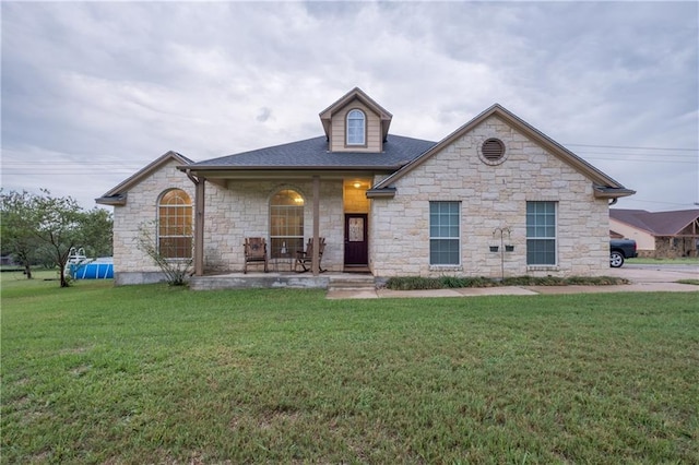 view of front of home with a front lawn, stone siding, and covered porch