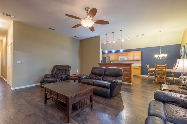 living area with ceiling fan with notable chandelier, baseboards, dark wood finished floors, and visible vents