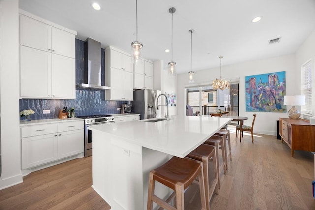 kitchen with an island with sink, wall chimney exhaust hood, visible vents, a sink, and stainless steel appliances