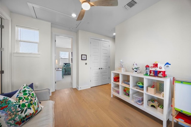 rec room featuring light wood-style floors, attic access, a ceiling fan, and visible vents