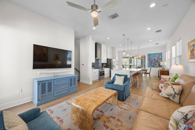living room with visible vents, light wood-style flooring, recessed lighting, and ceiling fan with notable chandelier