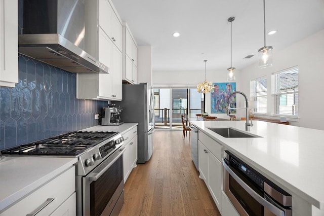 kitchen featuring wall chimney exhaust hood, a sink, light countertops, appliances with stainless steel finishes, and decorative backsplash