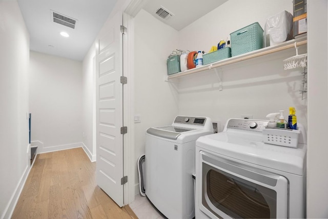 clothes washing area featuring visible vents, light wood finished floors, washing machine and dryer, and laundry area