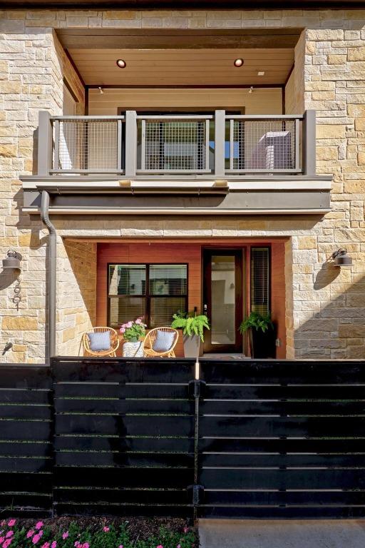 entrance to property featuring a balcony, stone siding, and fence
