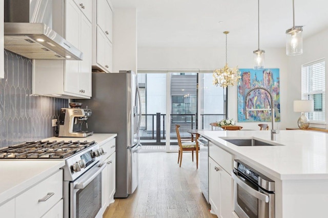 3901 Vantage Dr, Austin, TX 78731 - kitchen featuring wall chimney range hood, appliances with stainless steel finishes, a sink, light wood-style flooring, and a chandelier