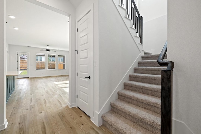 stairway featuring baseboards, a ceiling fan, and wood finished floors