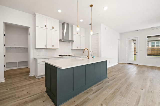kitchen featuring wall chimney range hood, tasteful backsplash, white cabinets, and gas stovetop