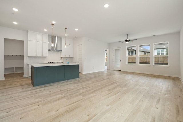 kitchen with light countertops, white cabinetry, a center island with sink, wall chimney exhaust hood, and light wood finished floors
