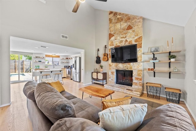 living room featuring visible vents, a fireplace, light wood-style flooring, a ceiling fan, and baseboards