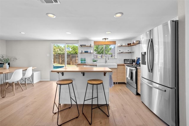 kitchen with a kitchen bar, a sink, open shelves, light countertops, and appliances with stainless steel finishes