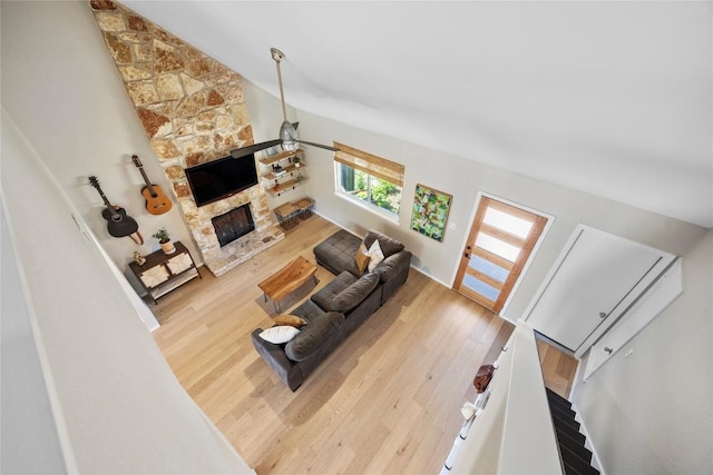 living area with wood finished floors, lofted ceiling, and a stone fireplace