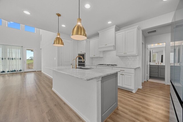 409 Dycus Bnd, Liberty Hill, TX 78642 - kitchen with a sink, white cabinets, recessed lighting, light wood-style flooring, and a kitchen island with sink