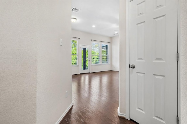hallway featuring dark wood finished floors, visible vents, and baseboards