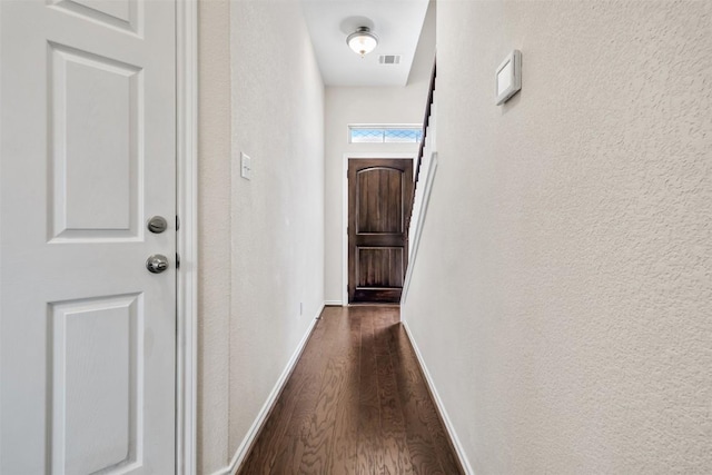 hallway with baseboards, a textured wall, visible vents, and dark wood-style floors