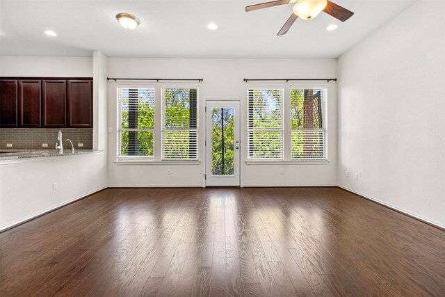 unfurnished living room with plenty of natural light, a ceiling fan, and dark wood-style floors