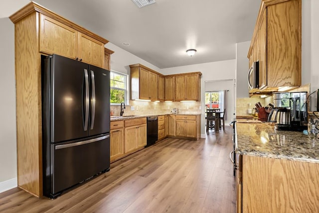 kitchen with light stone countertops, decorative backsplash, black appliances, and light wood finished floors