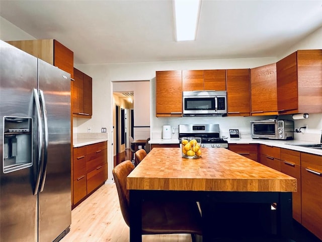 16903 Isle Of Man Rd, Pflugerville, TX 78660 - kitchen featuring appliances with stainless steel finishes, wooden counters, light wood-style floors, a kitchen island, and brown cabinets