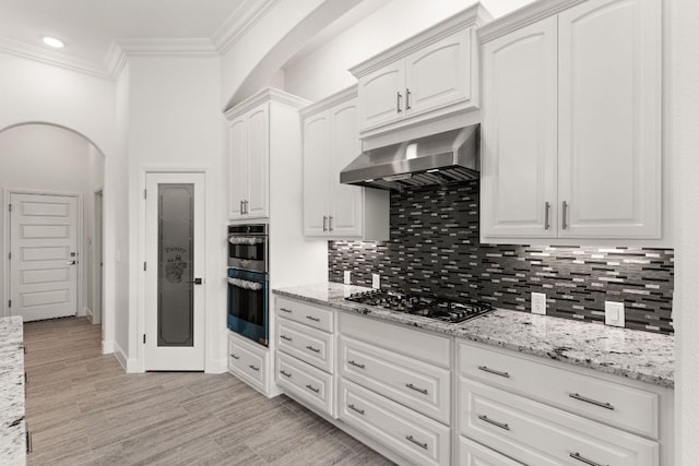 112 Vista De Luna Ln, Belton, TX 76513 - kitchen with appliances with stainless steel finishes, wall chimney exhaust hood, arched walkways, light stone counters, and ornamental molding