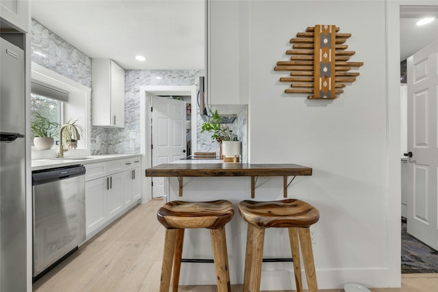 1616 Webberville Rd Unit A, Austin, TX 78721 - kitchen featuring appliances with stainless steel finishes, white cabinets, light wood-style flooring, a kitchen bar, and backsplash