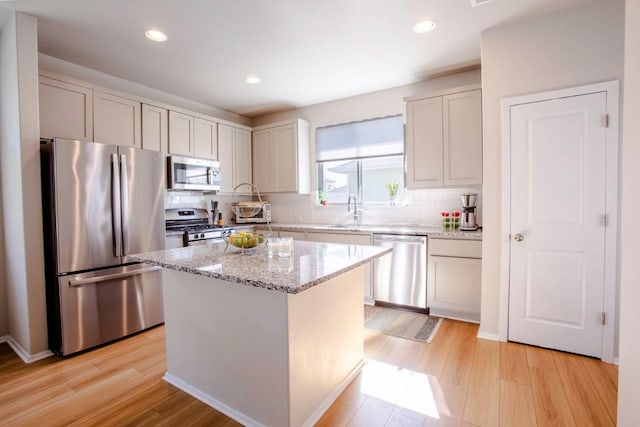 188 Catalina Dr, Kyle, TX 78640 - kitchen featuring light stone countertops, appliances with stainless steel finishes, a sink, light wood-style floors, and decorative backsplash