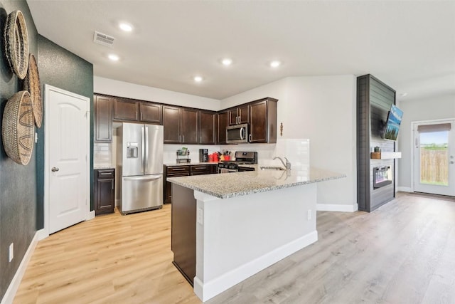 353 Cherry Laurel Ln, Kyle, TX 78640 - kitchen with stainless steel appliances, dark brown cabinets, light wood-style floors, a peninsula, and a sink