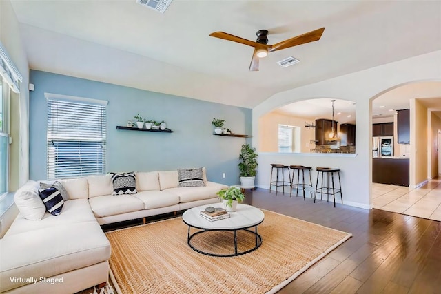 living area with light wood finished floors, arched walkways, ceiling fan, and a wealth of natural light