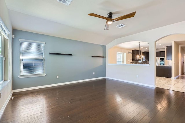 unfurnished living room with wood-type flooring, baseboards, arched walkways, and ceiling fan with notable chandelier