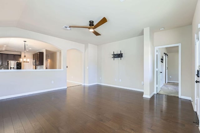 unfurnished living room featuring visible vents, baseboards, arched walkways, dark wood-style floors, and ceiling fan with notable chandelier