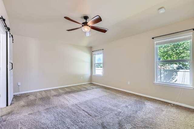 carpeted spare room with baseboards, a ceiling fan, and a barn door