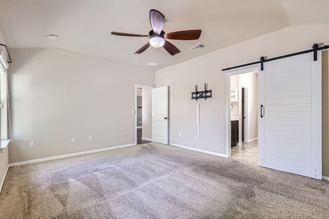 unfurnished bedroom with light carpet, ensuite bath, a barn door, visible vents, and lofted ceiling