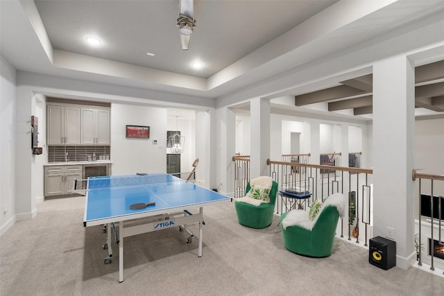 recreation room with baseboards, beverage cooler, ceiling fan, light colored carpet, and a raised ceiling